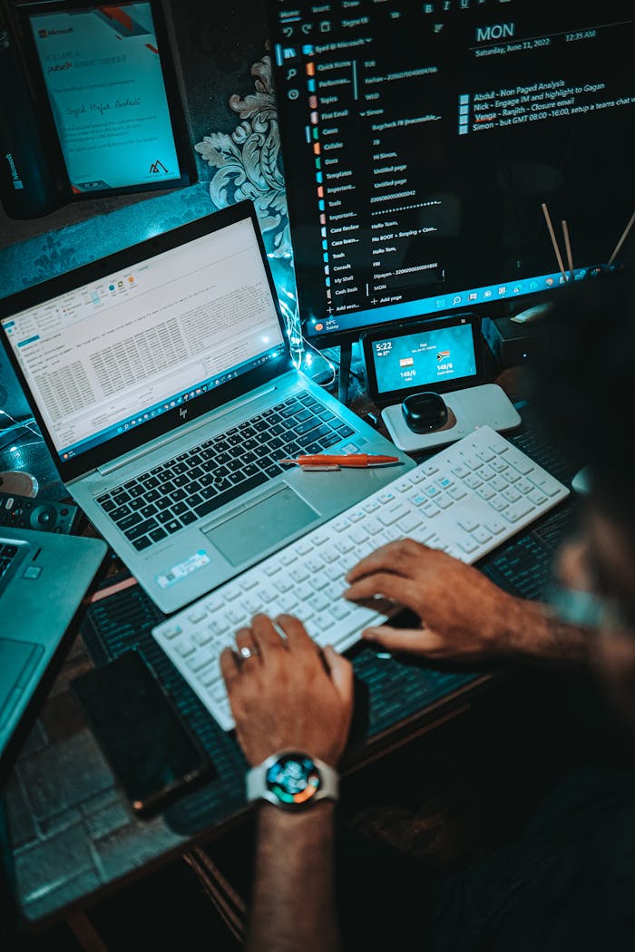 A person working on a dual-monitor setup with a laptop and keyboard in an office environment.